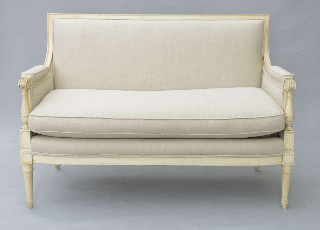 Settee, having distressed painted finish, fielded frame, square upholstered back, foliate carved scrolling arms with padded elbow rests, raised on turned stiles, drop-in down cushion; raised on round tapering legs. Upholstered in linen. Attributed