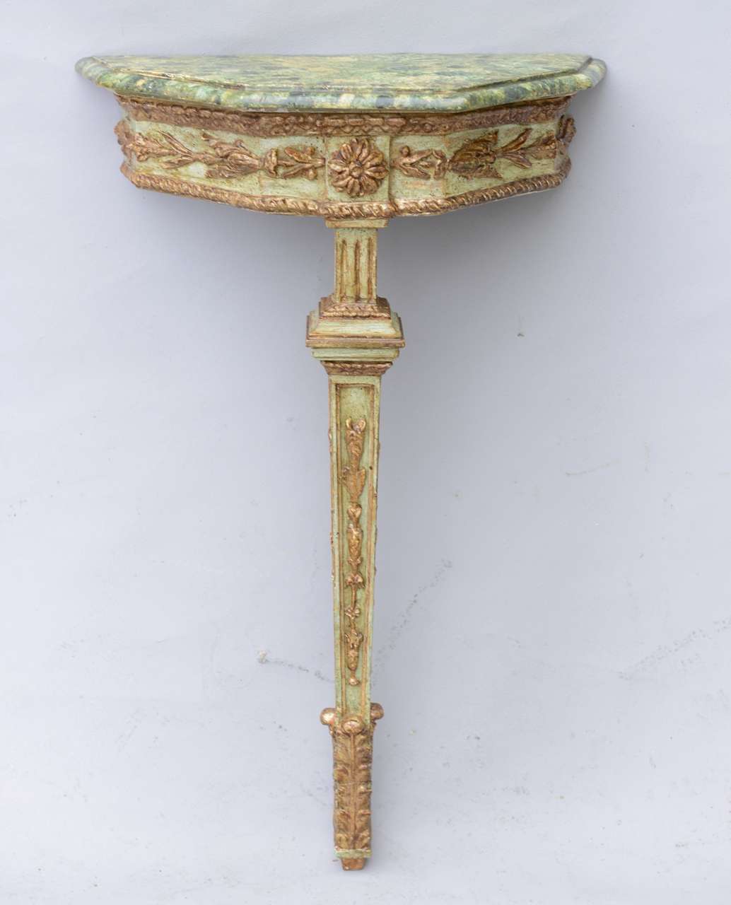 Pair of single leg, wall mounting, console tables, each having a green marbelized molded top with canted sides, on painted and parcel gilt conforming base, its apron centered with a rosette, flanked by laureling, raised on a fluted terminal,
