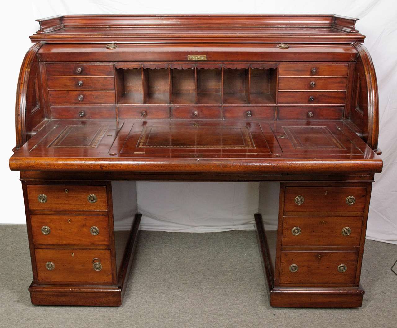 A c.1850 British Mahogany cylinder desk. The molded gallery top over cylinder roll revolving to reveal a fitted interior pull out writing surface with tooled leather inset, compartments over a double bank base, having graduated drawers rising on a