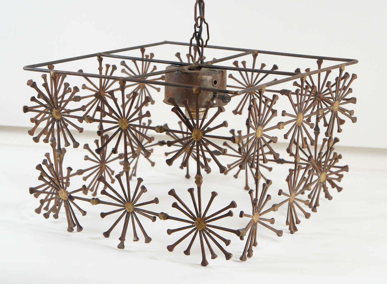 Here is a unique box shaped chandelier with a multiple sunburst pattern constructed of spike nails. This piece has a rustic patina with painted gold detail.