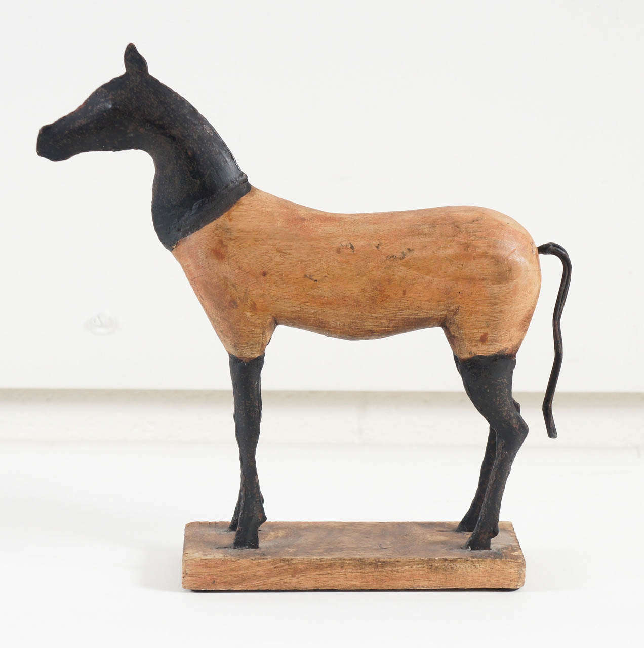 Here is a horse sculpture in a primitive style made of carved wood and blackened metal. The sculpture is mounted to a wooden base.