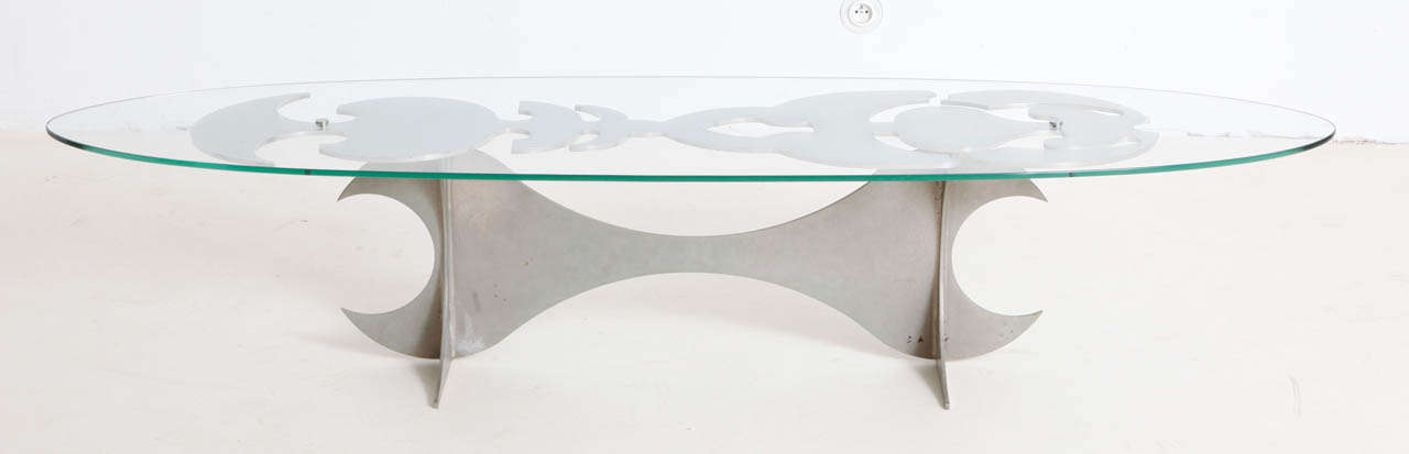 Coffee table featuring a base composed of a double pedestal base with shaped stitcher which holds a top support done in  a elongated abstract tattoo like pattern all in a polished chromed steel. This base holds an oval shaped thick glass top. By