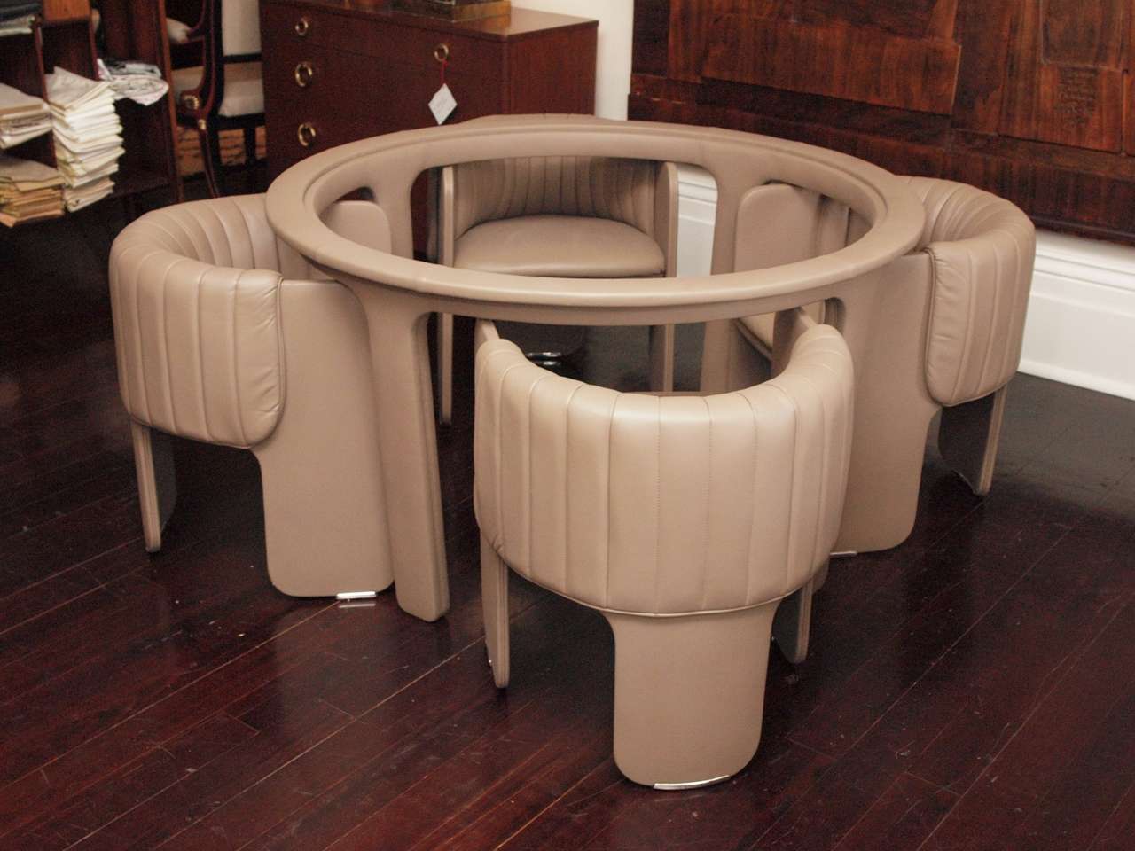 Round table with four tubs chairs by Poltrona Frau; each piece fully upholstered in taupe leather; the table bearing the maker's embossed mark at one leg; the chairs bearing metal labels under the seat; the chair backs  channel-quilted; the suite