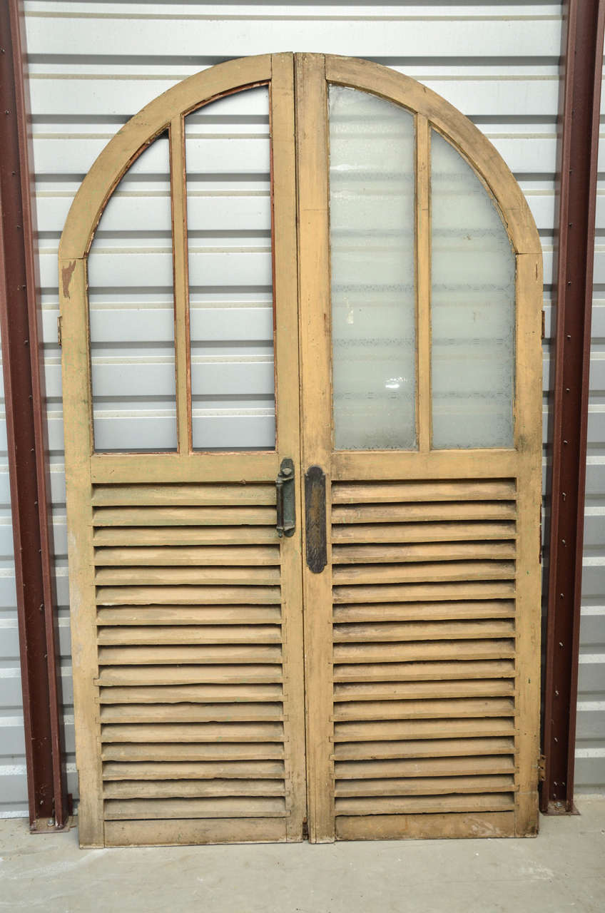 English Victorian arched double doors with etched (original frosted glass left on one-door) rectangular glass panels at top and louvered wooden panels below. The back of louvered panels are covered with solid panels.
Very decorative doors for a