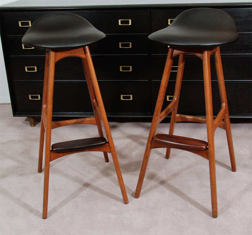 A pair of his-and-hers stools with newly reupholstered black leather seats on a teak base with rosewood foot rests. By noted designer Erik Buck.