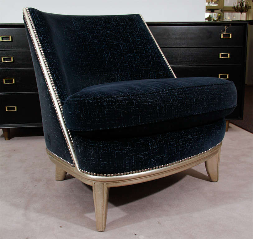 A pair of Art Deco style tub chairs modeled after those aboard the famed cruise ship Normandy. The pair have silver leafed frames with nailhead detailing and cut blue velvet upholstery.