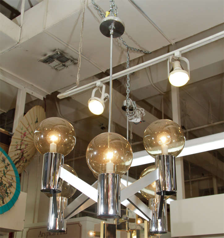 A Chrome frame chandelier with six illuminated glass globes set atop chrome cylinders that alternate in height.