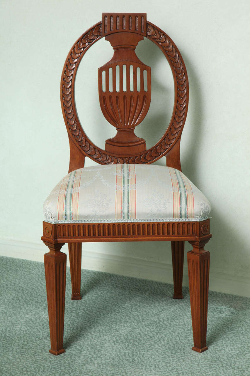Each with an oval shaped back carved with laurel wreaths centered by a fluted urn; the over-upholstered seat over a stop-fluted frieze on square tapering legs.