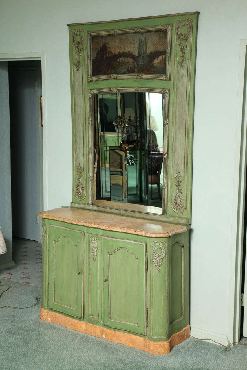 Possibly originally part of a paneled room.  The cabinet with peach marble top and faux marble painted base opening to a fixed shelf.  The mirror incorporating an oil painting on canvas depicting a river