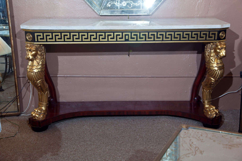 The extraordinary pair of console tables in the taste of Russian Neoclassical, circa 1920s, the white marble over a narrow frieze decorated with brass Greek key pattern, supported by two gilded lion pedestals with hoof feet, raised on a concaved