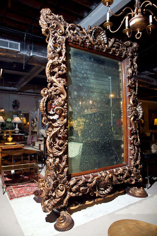 Monumental French Baroque style floor mirror, possibly first quarter of 20th century, stands enormously nearly 10 feet, the antique mirror surmounted by a wood frame of intricate carving of shells, scrolls, foliate, cartouche, etc., supported by two