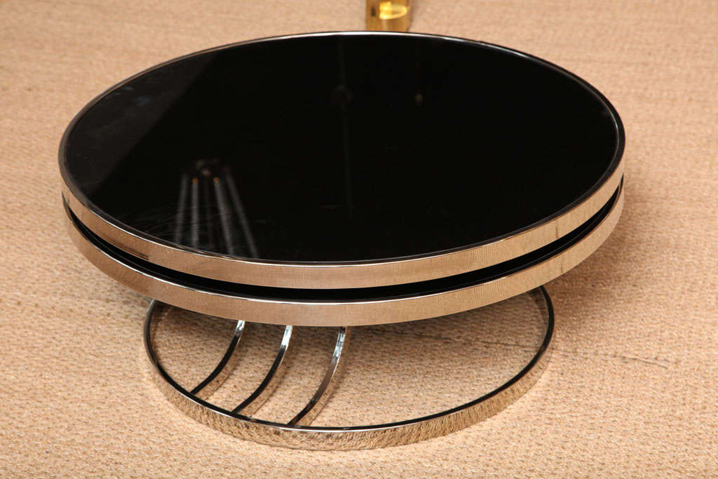 Two large discs in chrome and black painted glass swivel to create one circular cocktail table or opens to become a two-tiered table.  Modern Deco-like chrome base.  Original glass with crackled/marbled effect.