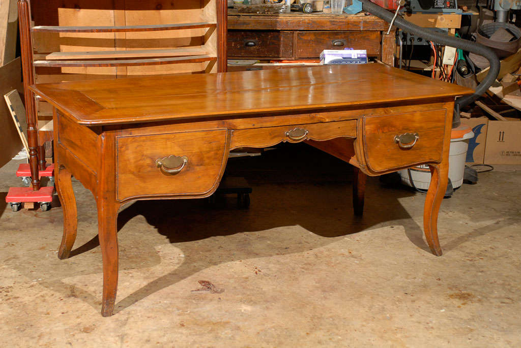 A provincial French fruitwood desk with 3 sliding drawers and false drawers on reverse side. All resting on curved saber legs. 
