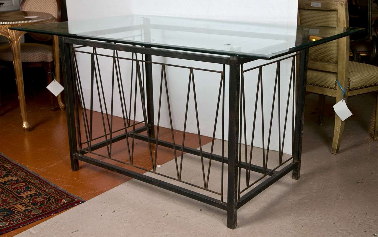 A finely cast metal base glass top desk in the style of Deigo Giacometti. The table measurements below the glass top measures 36'' X 60'' wide. The aged metal base having a solid framed V framed design center.