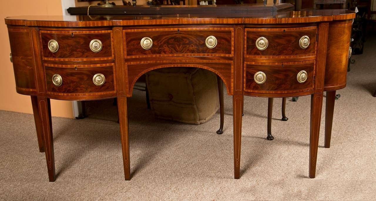 A fine inlaid and satinwood banded sideboard by the Baker Furniture Company. Tapering legs support this single banded drawer flanked by a pair of banded side drawers. The overall case piece having a serpentine front and demi lune sides all over