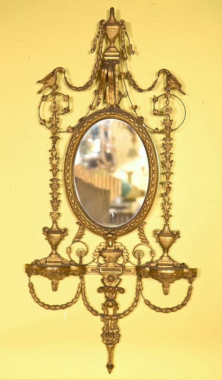 A pair of 19 century Adams Style gilt mirrors. Each oval mirror of fine antique quality having a central mirror w the top urn leading down to a flanking pair of birds with overall flowing vines and flowers. The lower portion having a pair of small