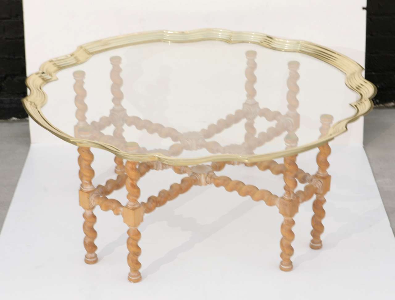 Brass edged glass piecrust coffee table on turned wood trestle base.