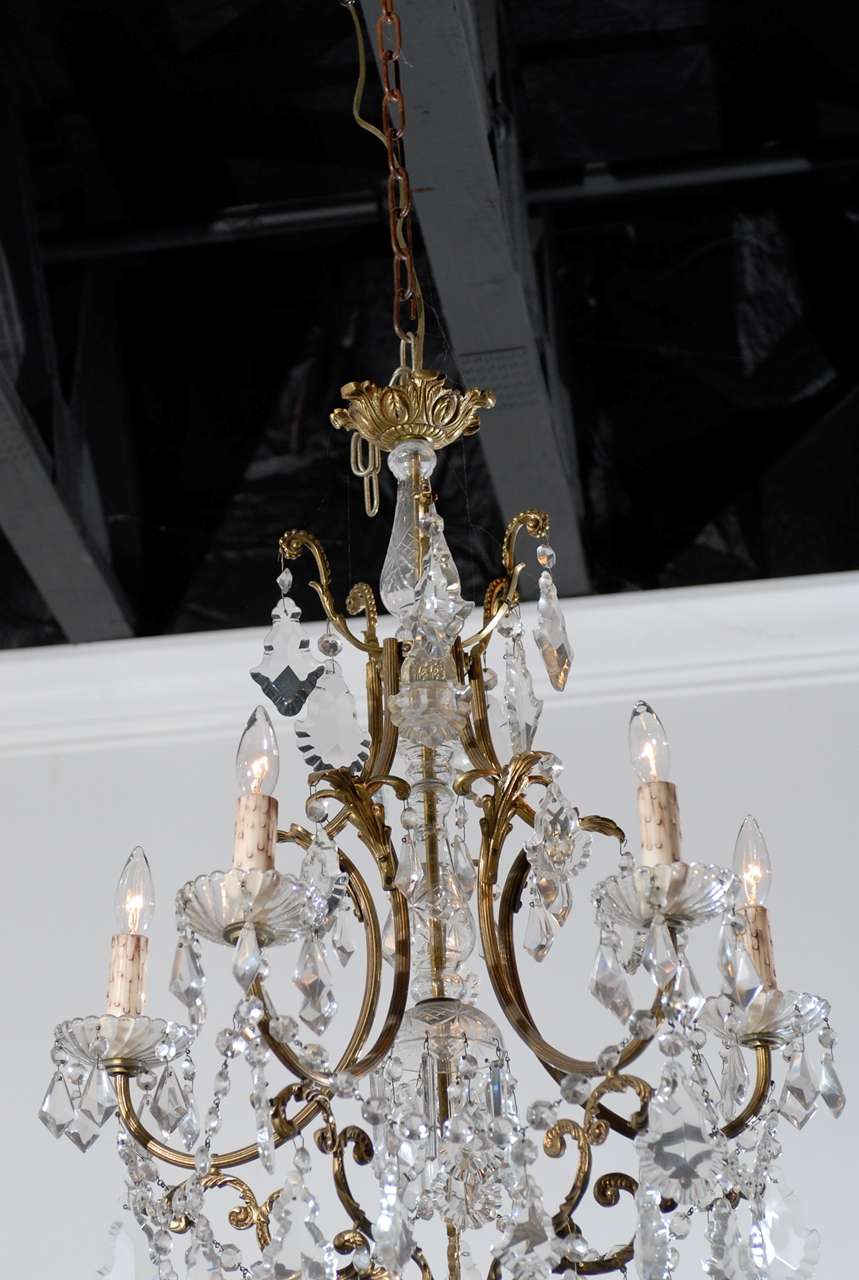 A French Rococo style, six-light chandelier with bronze armature and central glass column from the late 19th century. Typical of the rocaille taste developed under the reign of King Louis XV, this chandelier is all about curves, crystals and gold