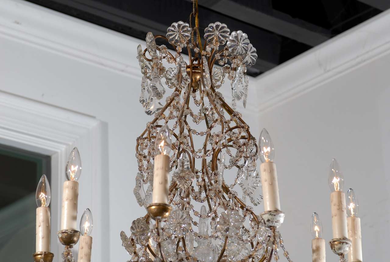 This Italian ten-light crystal Rococo style chandelier from the mid-19th century features a gilt, antique gold colored metal armature made of various scrolls and volutes. At the crest, s-scrolls support rosettes and pendeloques. The eye gently