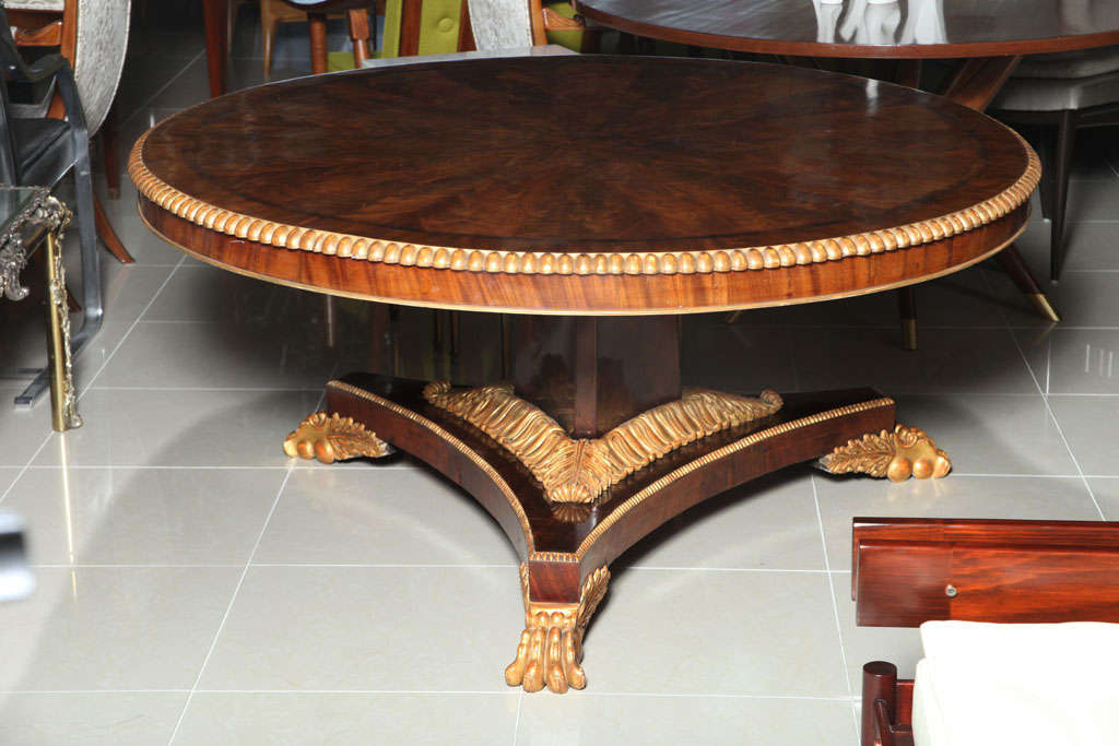 The radially veneered top with parcel-gilt edge above a pedestal on tripartite base carved with parcel-gilt acanthus resting on paw feet.