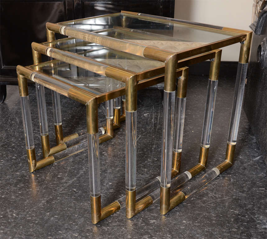 This stunning set of three nesting tables came from a prominent Palm springs estate. The tables are exquisitely designed with Lucite and brass frames  which have a beautiful patina. They have separate brass and glass tops, and are possibly Gabriella