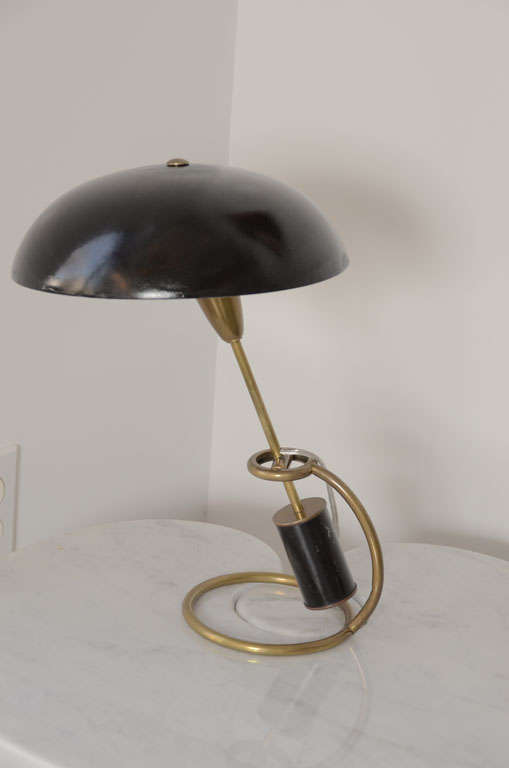 Italian adjustable table lamp by A. Lelli for Arredoluce.
Black round shade connected to a brass swivel arm standing on a brass bent base.