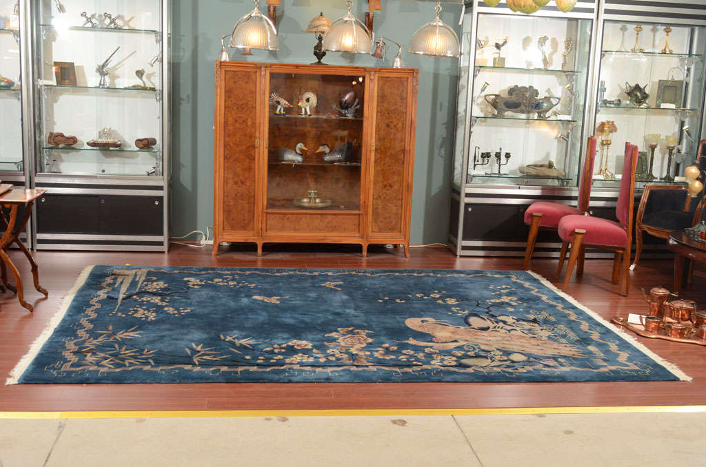 A fine and rare Peking Chinese Art Deco rug decorated with various flora, bamboo, butterflies, apple blossoms, moonscape with a stylized peacock against a bold and rich royal blue background. The rug is in excellent condition and age appropriate