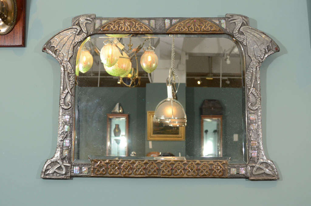 An Austrian Art Nouveau silvered and gilt repoussé mirror decorated with gargoyles and serpents, inlaid abalone, and red cabachon jeweled frame with its original beveled mirror.  glass mirror shows what appears to be flaking but this is how the