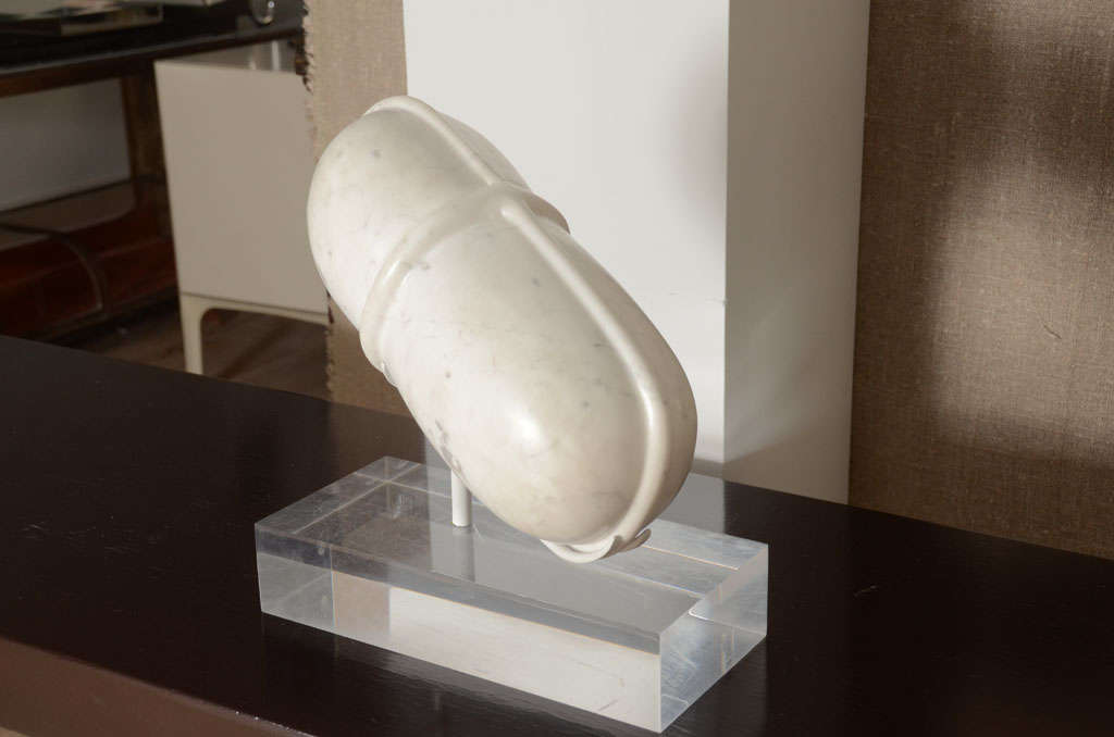 A Carrara marble sculpture of a pill with beautiful raised banding mounted professionally without drilling on a white metal stand and lucite base.