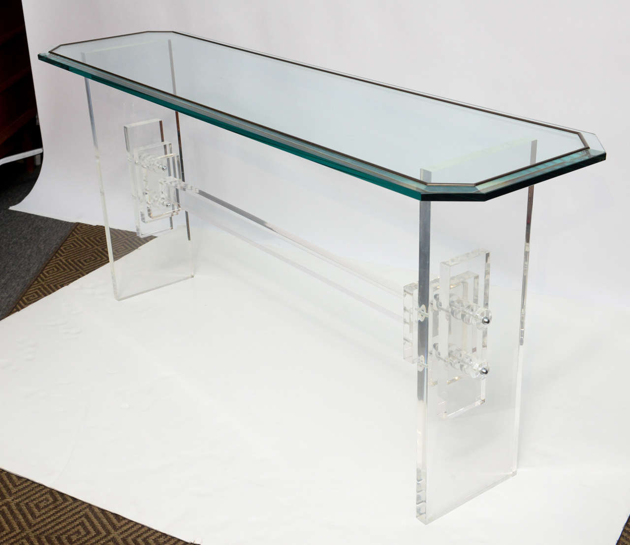 Simple and strong, this lovely acrylic table can light up any entrance. The table legs are graced with Art Deco inspired stacks of acrylic. The whole table is topped with a thick slab of glass cut in a long octagon with brass inlay. Tempered glass