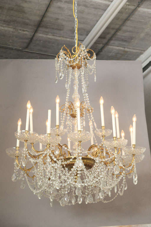 Sumptuous Louis XV-style gilt-brass and cut crystal 18-light chandelier; the cap issuing scrolling arms, joined by a double tier of faceted bead chains and centered by a drop pendant,  the glass-encased standard continuing to a circular shelf