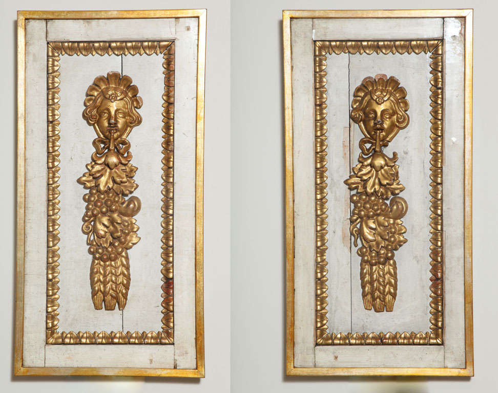 Pair of wall hangings, each antique fragment having painted and gilded frame with leaf detail, surrounding a classical carved giltwood face surmounting leaf and grape motifs.