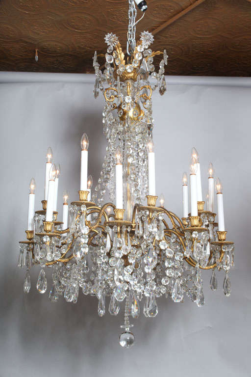 Louis XV-style gilt-bronze and cut crystal eighteen-light chandelier; its cap issuing leafy spires finished by cut class starbursts, joined by a strings of faceted bead chains and and drop pendants, the glass-encased standard emanating two-tiers of