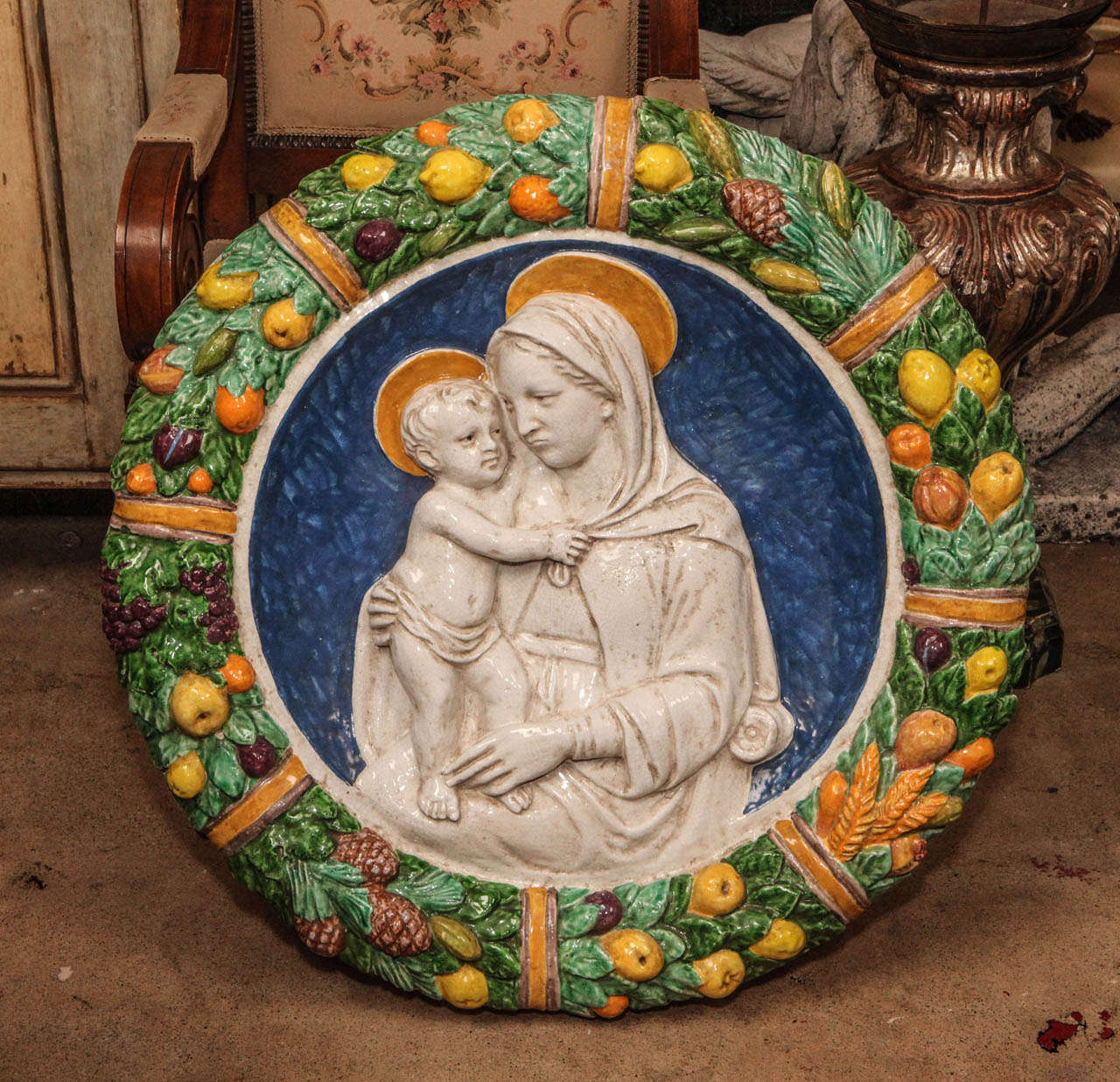Large, round, hand-painted, terracotta medallion of the Madonna and child, surrounded by a border of leaves and with fruit and flowers.