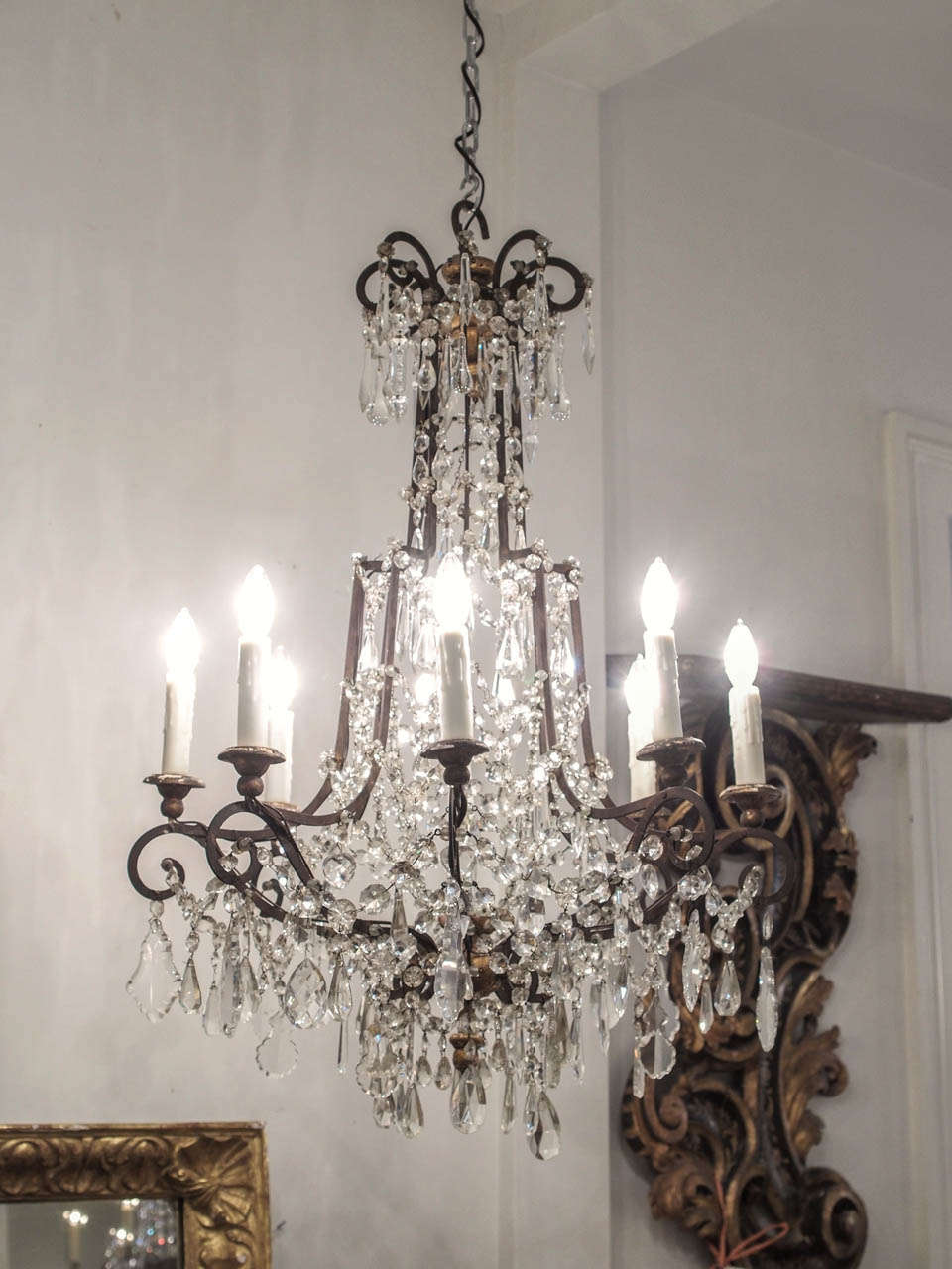 An eight light chandelier with scrolling tole arms joined by and terminating in carved and gilded finials.  This light displays an extraordinary assortment and sizes of crystals, from tear drop shaped to small faceted, and in between.