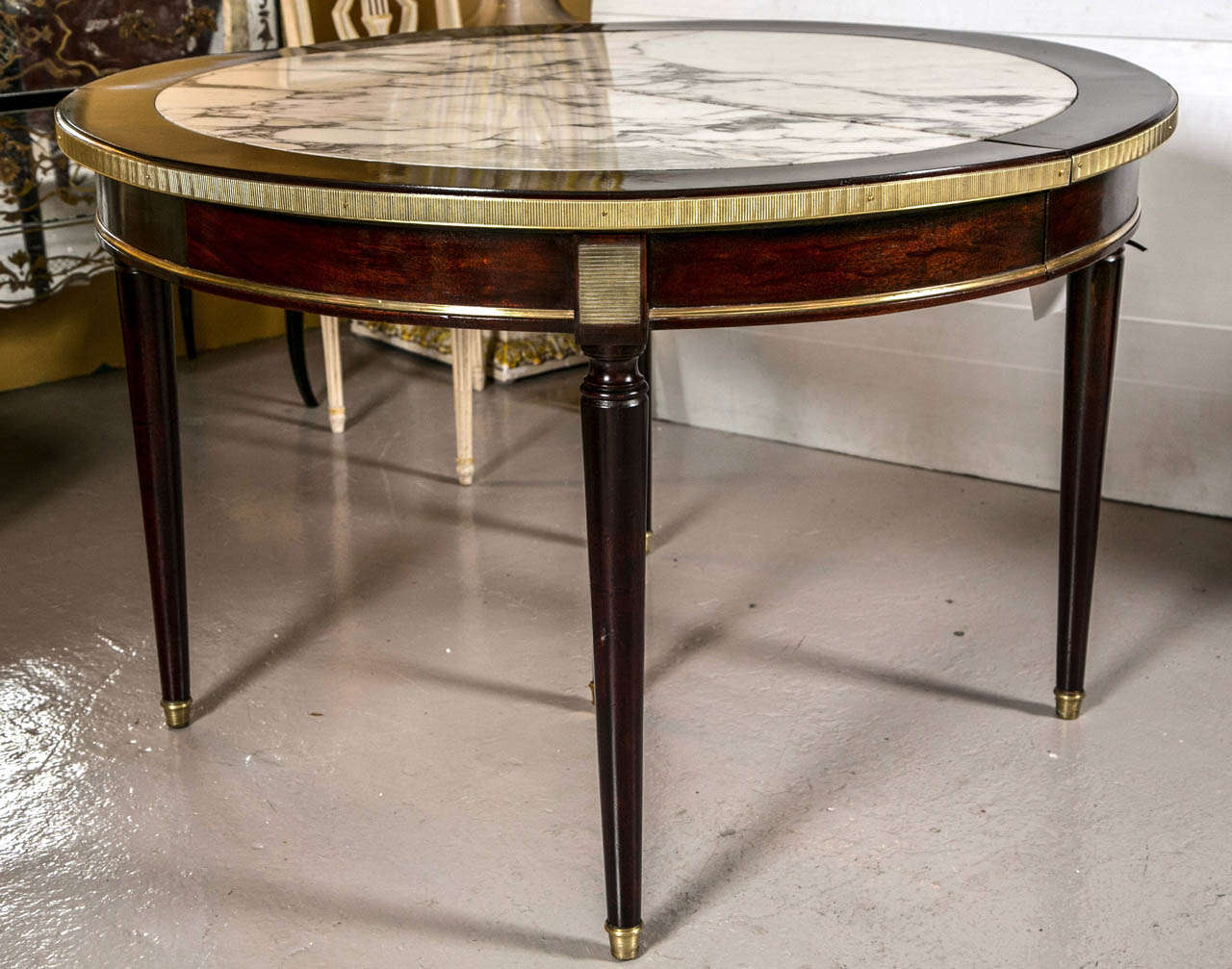 A one of a kind two leaf circular dining table by Maison Jansen. The fine Louis XVI Style tapering legs supporting a bronze mounted apron leading to a finely cast bronze mounted and framed mahogany table top. The top having four removable Carrera