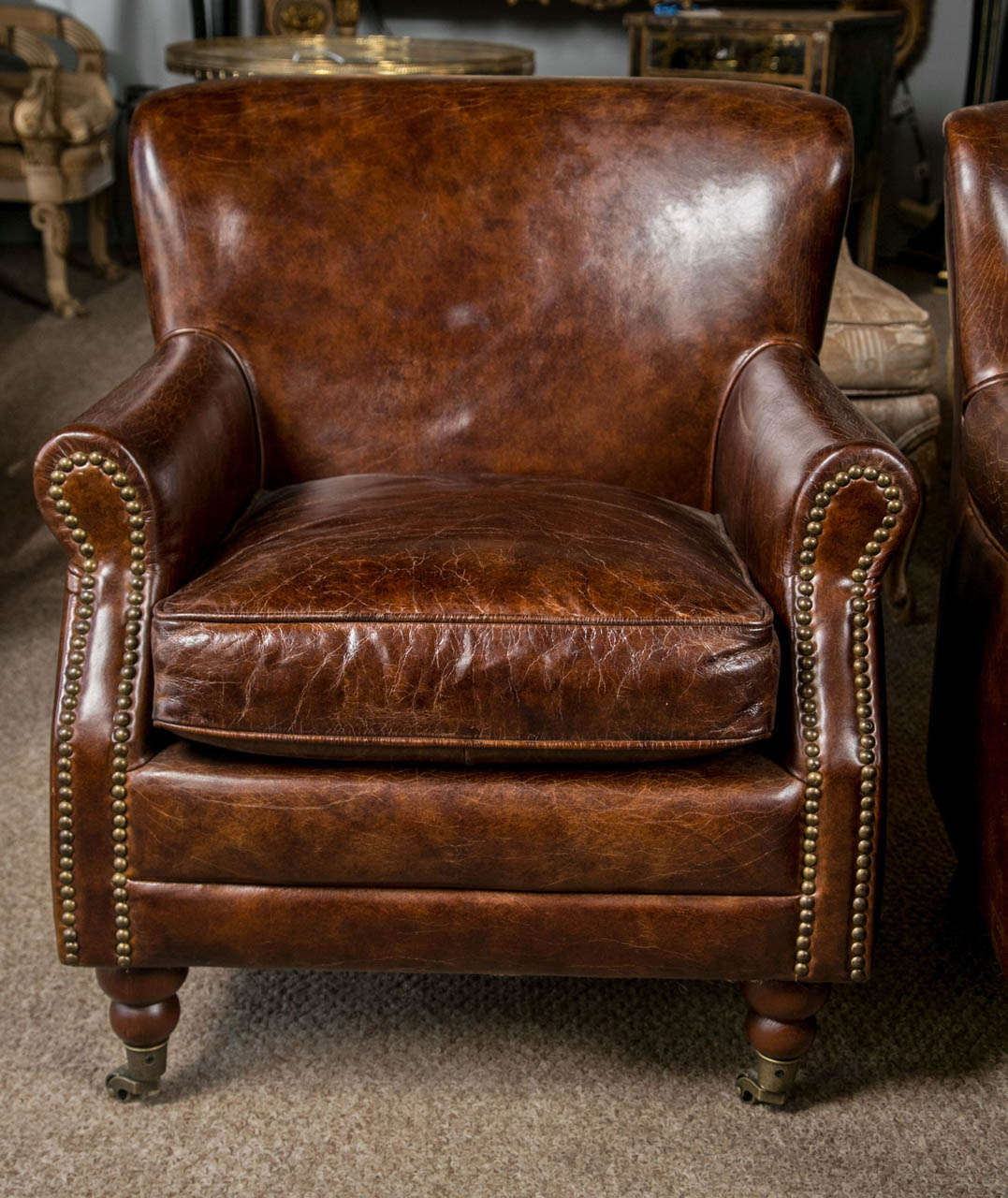 A fine pair of brown leather arm chairs. The whole of a worn brown leather in good condition with nail head arms resting on English ball bun feet and terminating in brass casters. At the time of this posting a group of four chairs are available.