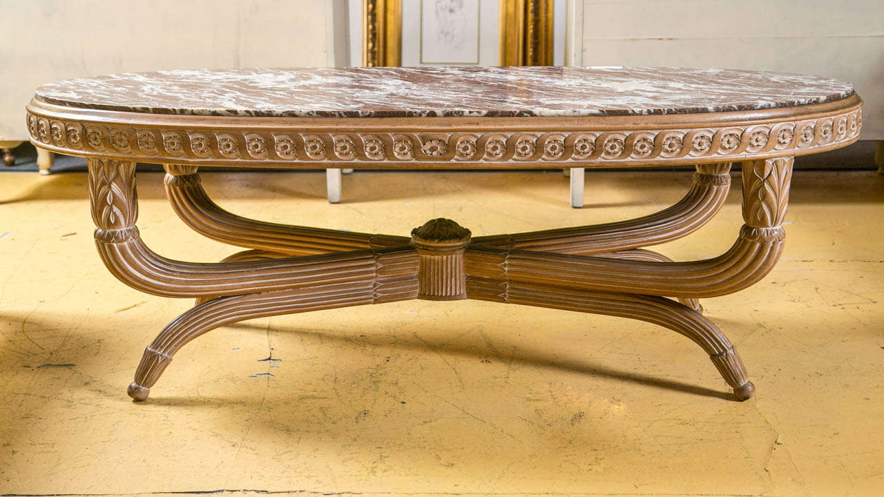 A finely detailed Hollywood Regency style coffee low table. The finish of a pickled wood look on an all-over carved and detailed frame terminating in a set of four pineapple carved capitols supporting a carved apron under a fine brown and white