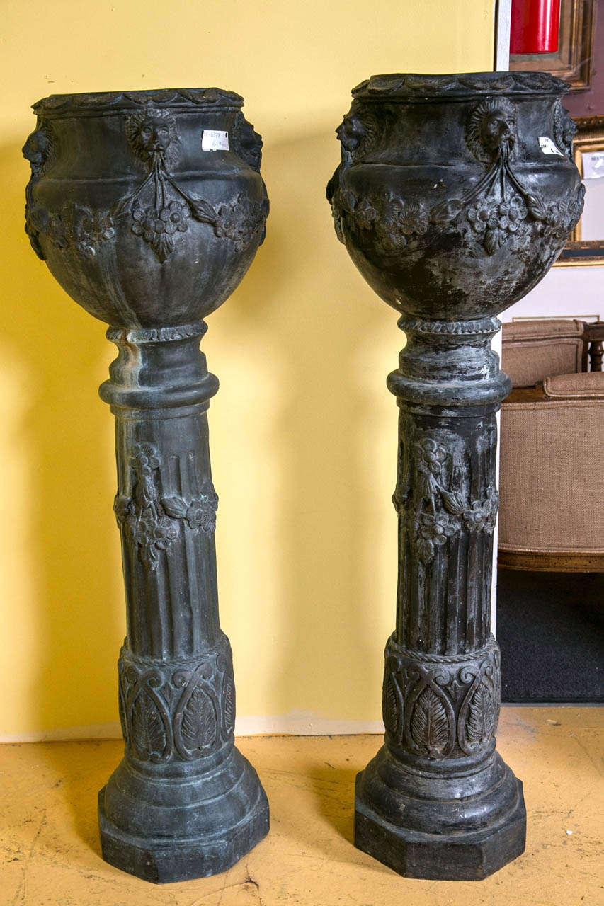 Pair of metal figural garden jardinares on pedestals. Each with a circular tubular base of bronze patination leading to an upper planter jardinière with figural lions and flowing drape and tassel design.