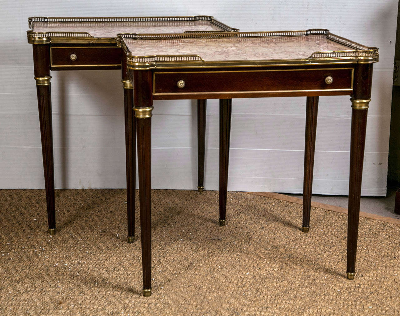 A Pair of French Louis XVI style End Tables. The bronze sabots leading to a group Louis XVI legs terminating in bronze caps. The pair having a single center drawer under a pierced bronze galleried marble top. by Maison Jansen