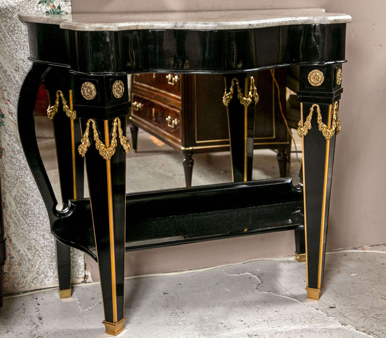 A fine pair of ebonized Maison Jansen mirrored back consoles. Each tapering leg having bronze mounts leading to a serpentine front and side console with a white marble top. The tops having been previously supported with a later central