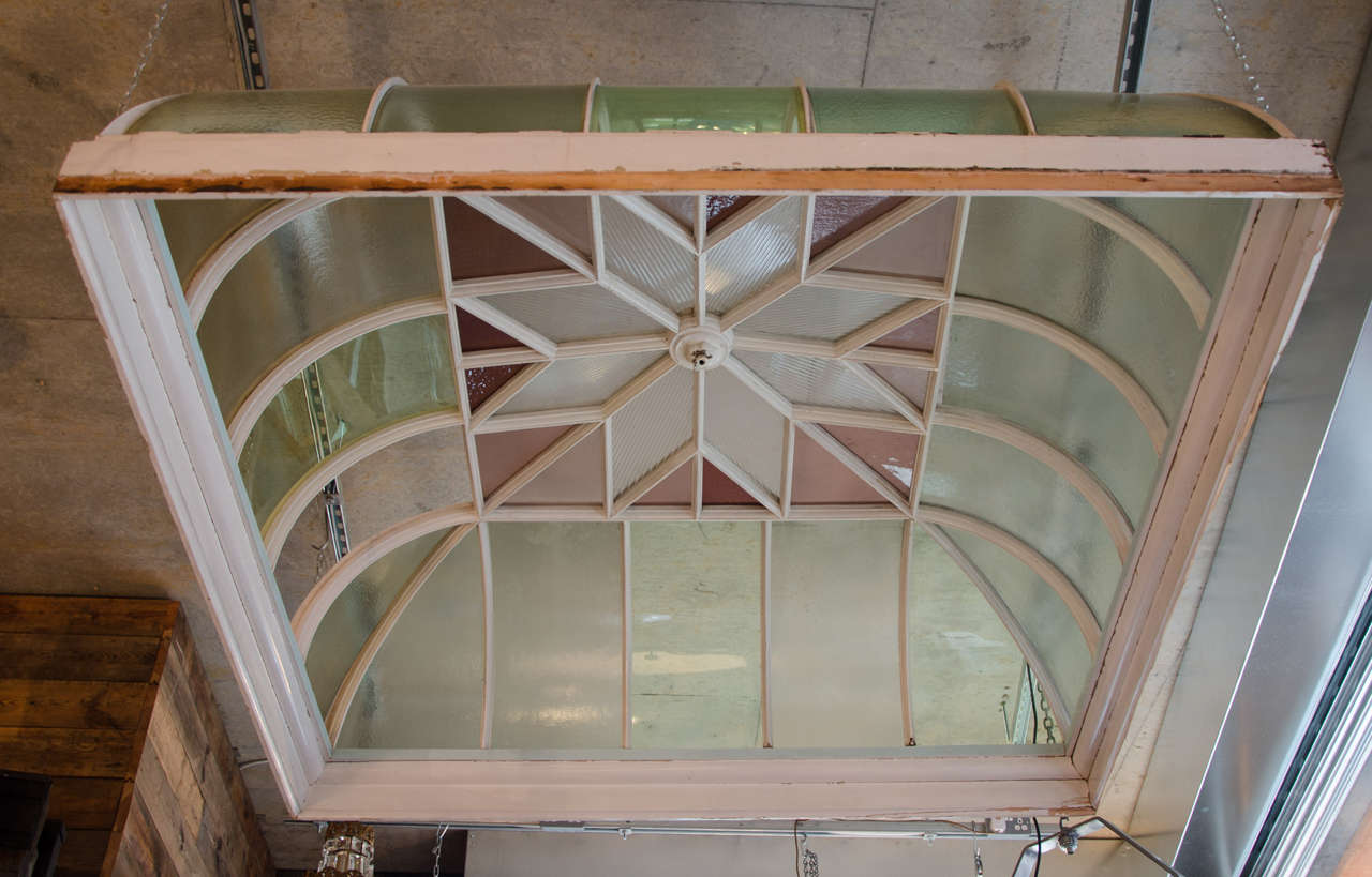An original antique skylight dome with a timber frame and stained glass panes. The skylight dome has a geometric design with a star design in the centre surrounding by soft plum shades of stained glass, and various shades of soft green, curved panes