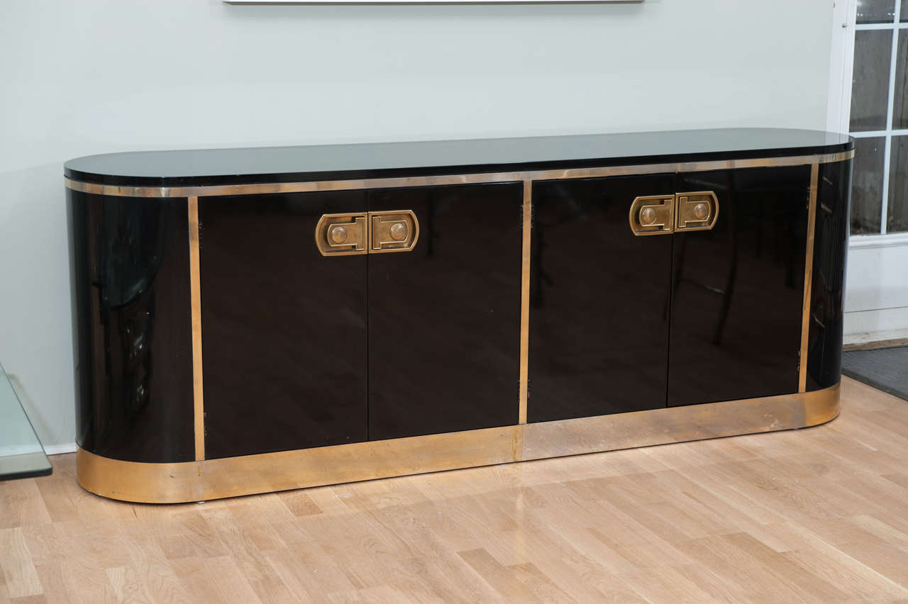 A glamorous black lacquered
oval credenza with brass plated trim and hardware.