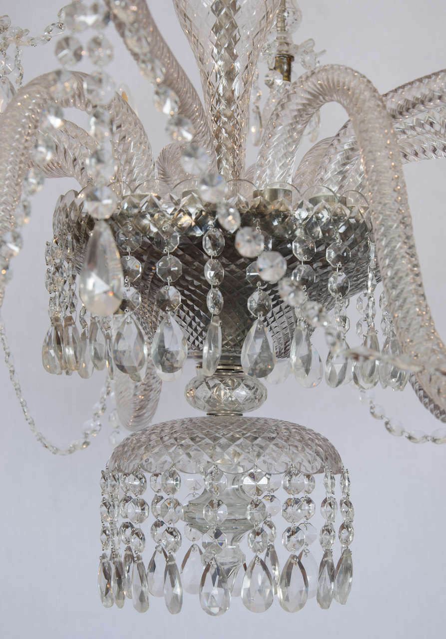 An opulent and stunning two-tiered crystal and glass chandelier is a 20th century light designed in the Georgian style. Each tier of the chandelier has six arms with candle shaped tapers and lights. The light measures 64 in–163 cm in total length