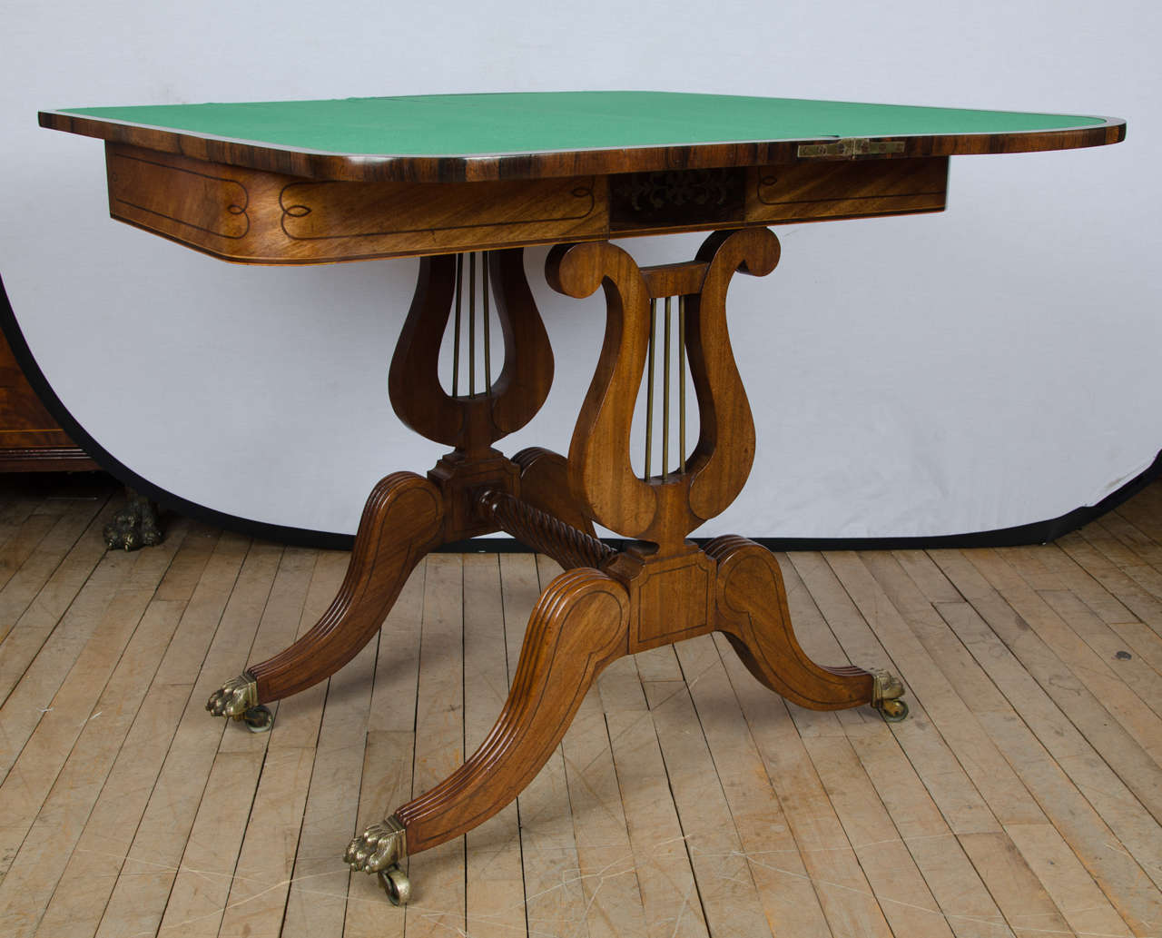 A superb quality Regency mahogany card table supported by 2 lyre sides and joined by a turned, twisted stretcher base ending on hairy paw brass castor feet. The table features a rosewood panel in the center of the frieze with a detailed brass inlay