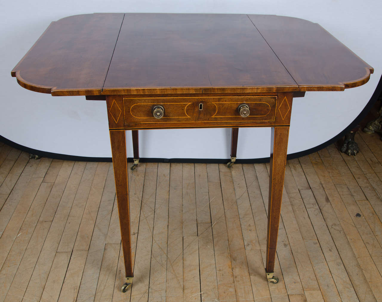 A Splendid Georgian mahogany Pembroke table inlaid and cross banded with Satinwood. The table features shaped leaves and boxwood stringing on the border of the cross banding. The Pembroke stands on square tapered legs with brass caps and castors. It