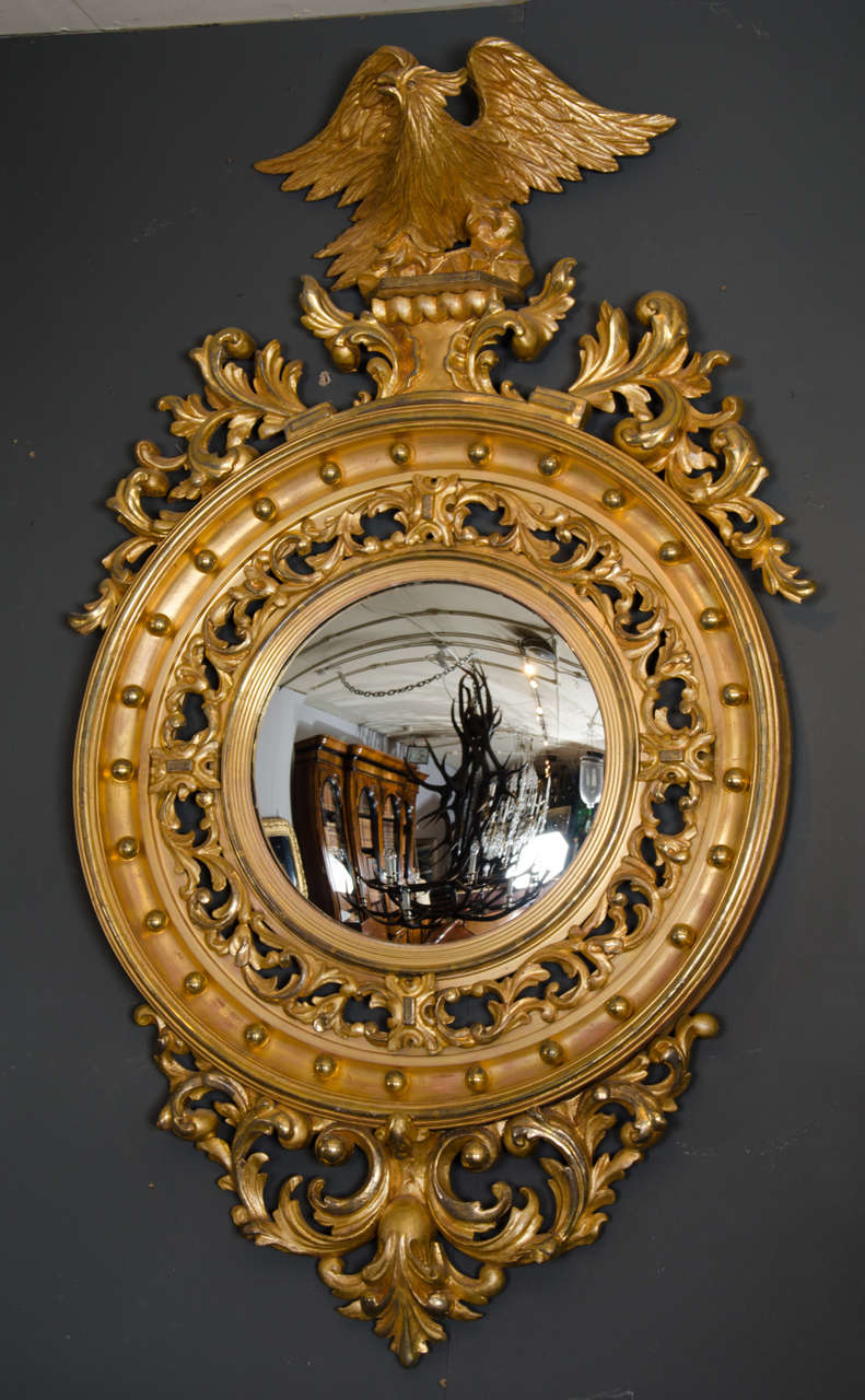 This outstanding late 19th C. Regency style round convex mirror features an extensively detailed carved gilt wood frame with a spread eagle pediment and embellished with acanthus leaf decoration around the bottom. The mirror measures 54 in – 137 cm