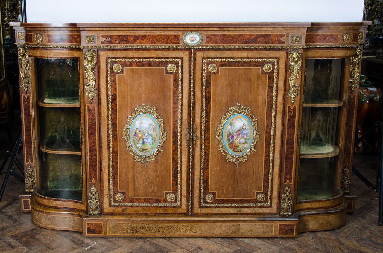 A very good quality mid-19th century Walnut  credenza having Amboyna cross banding, gilded ormolu mounts, shaped glass doors to either side and French 'Sevres' style porcelain plaques to the doors and frieze. Raised on a plinth base.