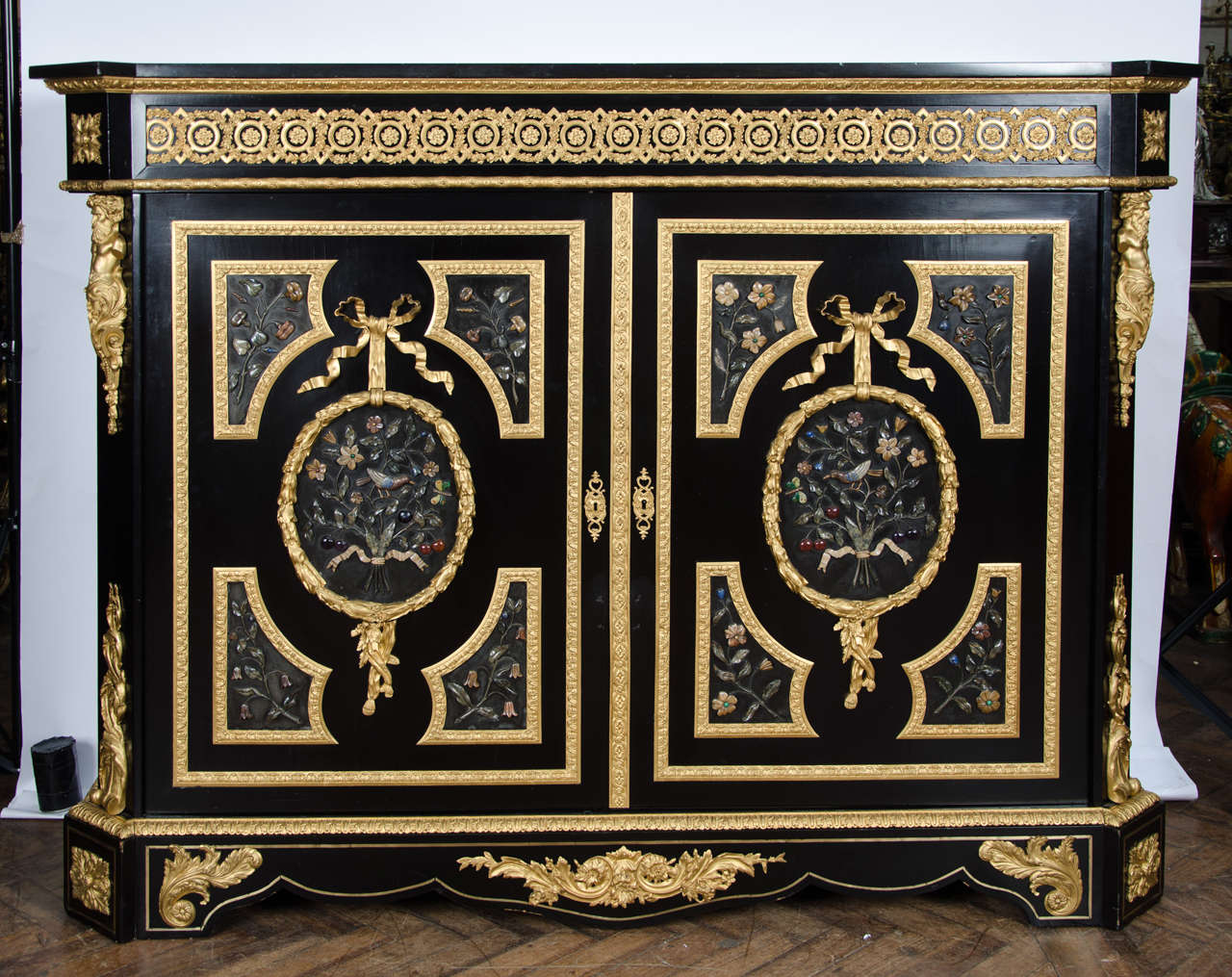 A very imposing and good quality French ebonized ormolu-mounted two-door cabinet having five panels of hard-stone relief depicting flowers and birds and raised on ormolu-mounted bracket feet.