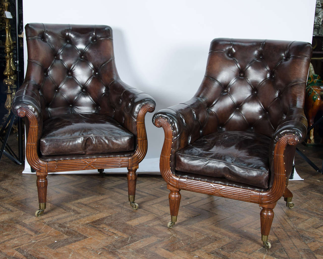 A very good quality pair of early 19th century mahogany library chairs, upholstered in deep button hide. The lyre shape having reeded carved decoration, raised on turned tapering legs, terminating in the original brass cup castors.